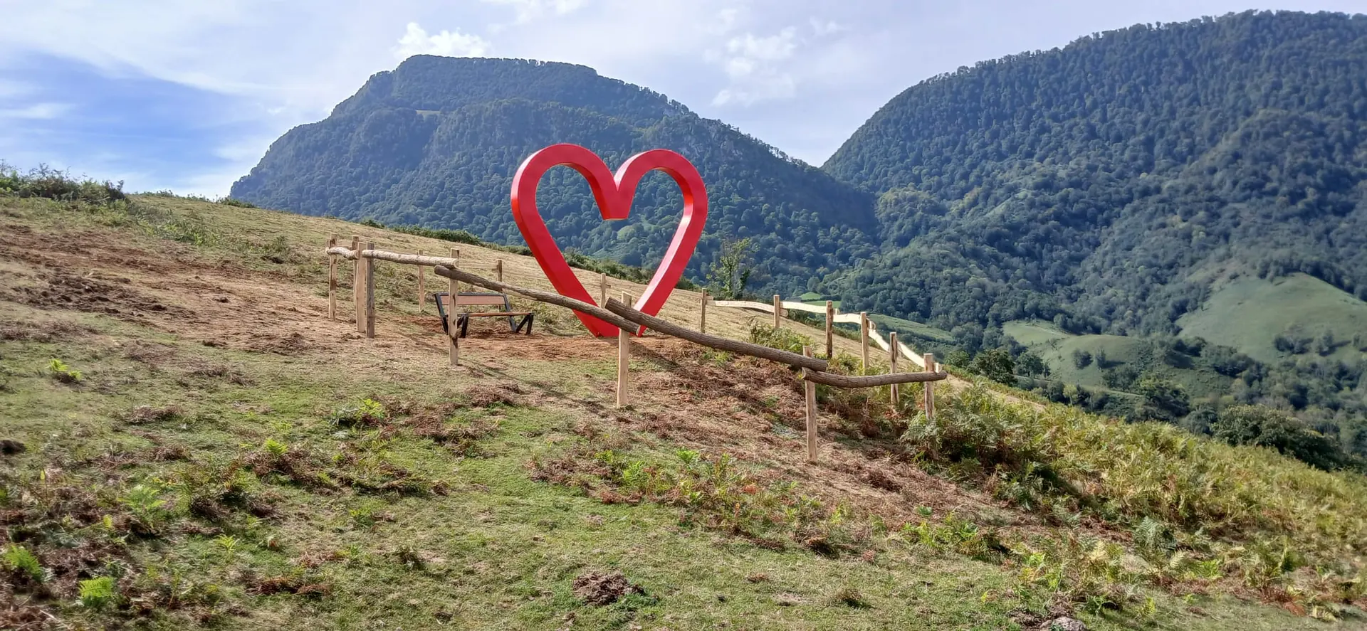 Sculpture d'un grand cœur rouge sur les hauteurs, face aux montagnes